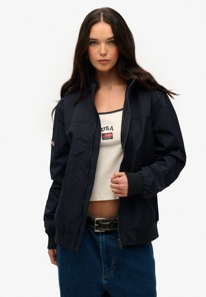 Marine capuchonjack met rits, met een staande kraag, ribgebreide manchetten en zoom. Bevat een logopatch op de linker mouw en is gemaakt van een gladde, lichtgewicht stof.