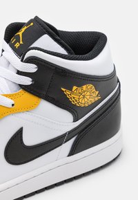 Černé a bílé sneakersy z umělé kůže se žlutými akcenty, s logem Air Jordan, texturovanou tkaninou a kulatými tkaničkami.