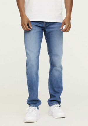 Jeans en denim bleu clair à coupe droite, avec un léger délavage et un aspect légèrement usé. Associés à des baskets blanches.