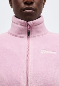 Κοντινό πλάνο ενός ατόμου που φοράει ένα ροζ ανοιχτόχρωμο fleece μπουφάν Berghaus με φερμουάρ, εμφανίζοντας τον γιακά και την περιοχή του στήθους.