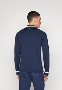 Sweatshirt azul-marinho com detalhes brancos na gola e nos punhos, apresentando textura canelada e um logótipo nas costas.