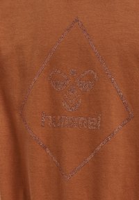 Bronsfärgad textil med en diamantformad design, en texturerad logotyp och glittriga accenter, vilket skapar ett visuellt distinkt mönster.