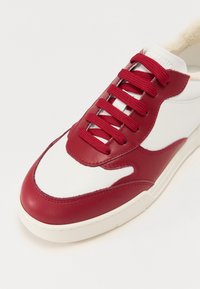 Piros és fehér bőr sneakerek, texturált felsőrésszel, kerek orral és kontrasztos cipőfűzőkkel. Puha bélés és gumi talp jellemzi.