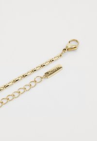 Bracelet en ton or avec un design en chaîne, fermoir à pince de homard et une étiquette rectangulaire gravée "LACOSTE".