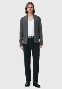 Cardigan gris en tissu doux avec un devant ouvert, porté sur un t-shirt blanc à col rond. Associé à un jean noir ample et des bottes noires.