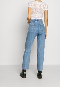 Jean taille haute bleu clair avec une coupe droite, dotés de poches arrière et de détails délavés. Associé à un haut en dentelle blanc à manches courtes.