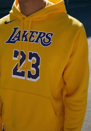 Gelbe Kapuzenjacke mit "LAKERS"-Logo und der Nummer "23" in lila und weiß, getragen von einer Person im Freien.