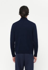 Ναυτικό πλεκτό πουλόβερ με ψηλό γιακά και μακριά μανίκια. Διαθέτει ριμπ μανσέτες και στρίφωμα. Υποτονική υφή, χωρίς ορατά λογότυπα ή σχέδια.