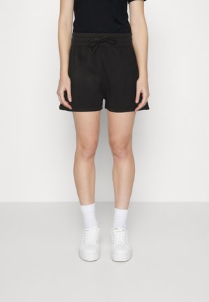 Zwarte katoenen shorts met een elastische tailleband en trekkoord, met een ontspannen pasvorm en zijnaad, gecombineerd met witte sneakers en sokken.