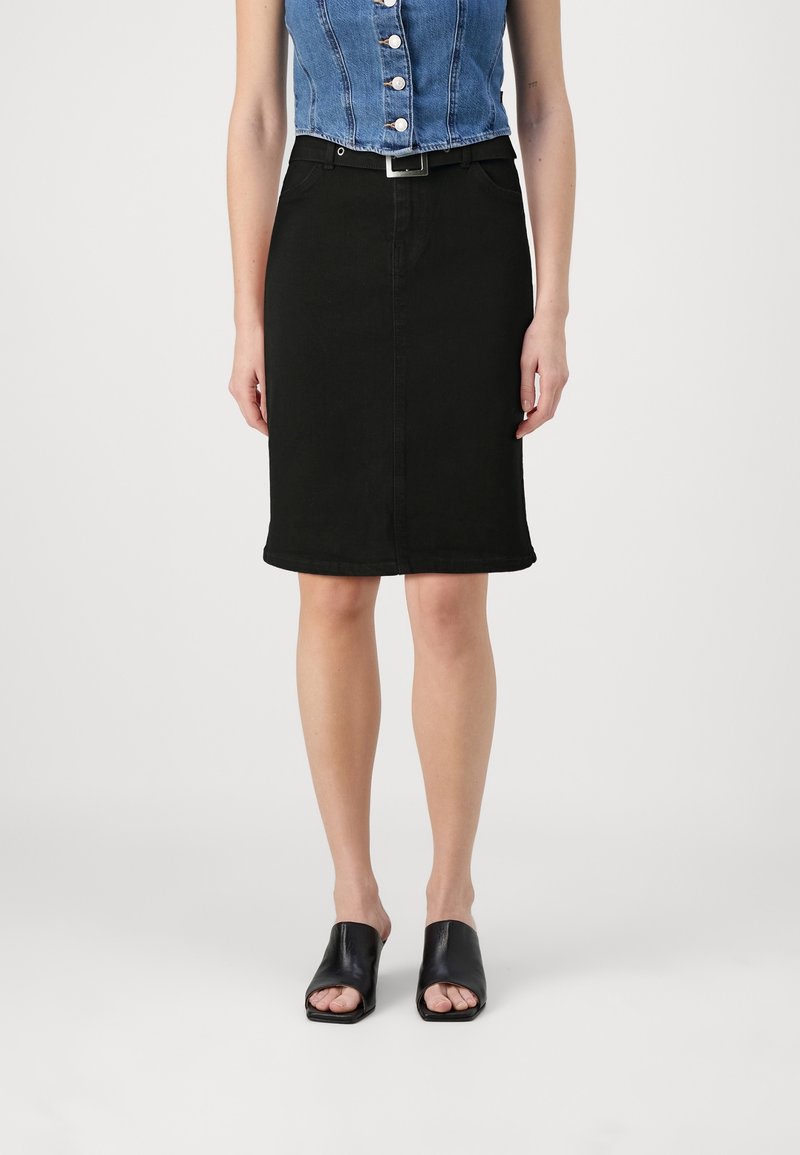 Falda lápiz de denim negra con corte recto y dobladillo, que cuenta con trabillas para cinturón y bolsillos laterales. Se lleva con sandalias negras de punta abierta.