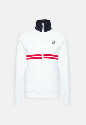 Chaqueta blanca con cremallera y cuello azul marino, con dos franjas horizontales rojas en el pecho y un logo en el lado izquierdo.