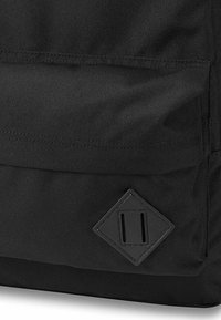 Zaino in tessuto nero con superficie testurizzata, toppa in pelle a forma di diamante con due fessure verticali e dettagli di cucitura in evidenza.