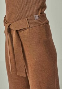 Braune Strickhose mit hohem Taillenbund und gebundenem Gürtel. Verfügt über ein kleines Logotag und eine glatte Textur. Seitliche Ansicht dargestellt.