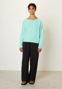 Lyse teal oversized sweater med en bred halsudskæring og lange ærmer, parret med sorte vide bukser og brune flade sandaler.