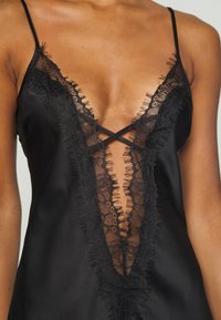 Satin black camisole with deep V-neck, featuring delicate black lace trim and frayed edges along the neckline and straps.