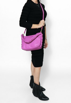 Borsa a tracolla rosa con manici intrecciati, materiale a superficie liscia e spallaccio staccabile, abbinata a un abito nero aderente e stivaletti alla caviglia con frange.