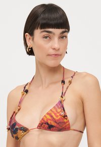 Triangelbikini med färgglad, abstrakt mönster i orange, lila och blått. Har knutna remmar och dekorativa pärlornament.