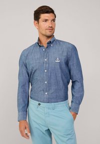 Blauwe chambray overhemd met lange mouwen en een logo op de borst; gecombineerd met lichtblauwe broeken; zachte textuur en op maat gemaakte pasvorm.