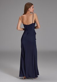 Robe longue bleu marine avec des bretelles spaghetti, un corsage ajusté et une jupe évasée. Tissu lisse avec un léger éclat, dotée d'une fermeture éclair dans le dos.