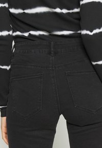 Persona vistiendo jeans negros de cintura alta con bolsillos traseros y una camiseta de rayas blancas y negras de manga larga, mostrada desde la cintura hacia abajo.