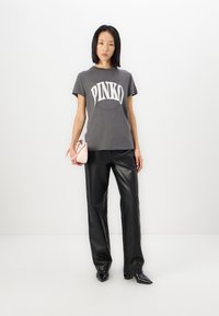 Camiseta de algodón gris con el logo "PINKO", combinada con pantalones de piel sintética negros y botas negras de punta, sosteniendo un mini bolso rosa claro.