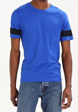 Camiseta de algodón azul con rayas negras en las mangas cortas, cuello redondo y diseño ajustado. Combinada con jeans de mezclilla azul.
