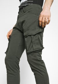 Olijfgroene cargobroek met meerdere zijzakken, slim fit, gemaakt van lichtgewicht stof, met knoopsluiting en stiksel-details.