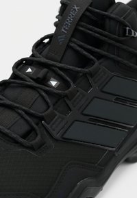 Schwarzer Adidas Terrex Wanderschuh aus Gore-Tex-Material, mit detaillierter Schnürung und markantem Drei-Streifen-Design auf weißem Hintergrund.