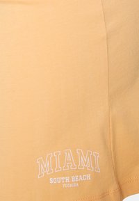 Camiseta de algodão laranja clara com um logotipo impresso em branco que diz "MIAMI SOUTH BEACH FLORIDA" em um layout arqueado. Textura suave.