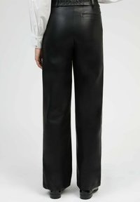 Pantalons large en cuir noir avec une texture lisse, dotés d'une poche arrière et d'un léger brillant, assortis de chaussures noires.