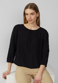 Zwarte blouse met een ronde halslijn, driekwartmouwen met elastaic manchetten en zachte, gladde stof. Gemaakt met lichte broek.
