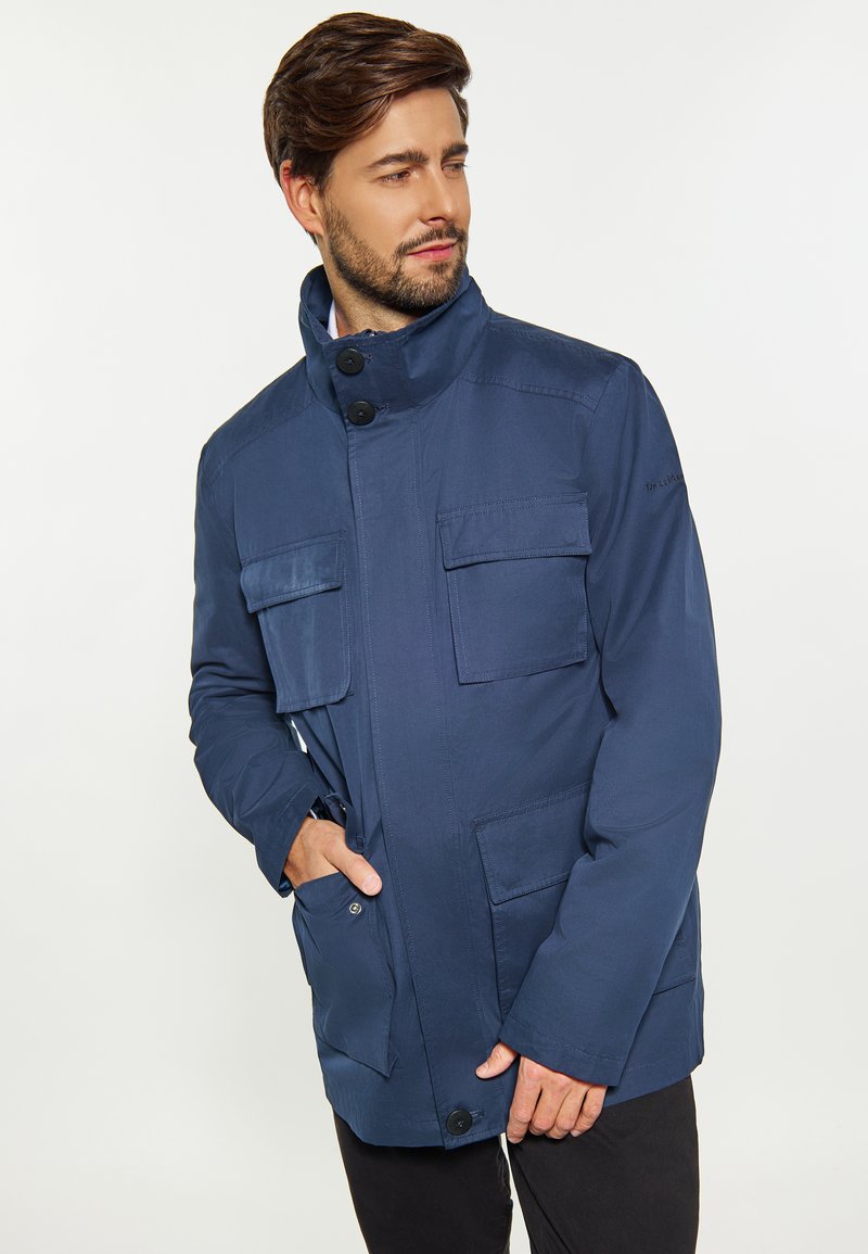 Navyblaue Utility-Jacke mit hohem Kragen, vier Fronttaschen, Knopfverschluss und einem glatten, strukturierten Stoff.