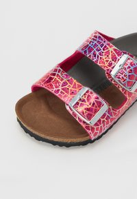 Ružové sandále s trblietavým, multikolórovým prasknutým vzorom, vybavené dvoma nastaviteľnými striebornými prackami a hnedou textúrovanou stielkou.