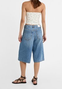 Culottes de mezclilla azul claro con un corte relajado, que cuentan con cuatro bolsillos y un dobladillo deshilachado. Combinados con un top corto floral ajustado y sandalias con tiras.