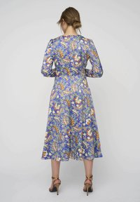 Langärmelig jurk in het blauw met een bloemen- en paisleyprint, met een getailleerde taille en een vloeiende rok. Gedragen met sandaaltjes met hakken.