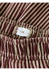 Stripet stof i bordeaux og beige, med en samlet talje med synlig søm og en hvid knaplukning.