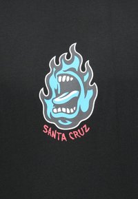 Φωνάζουσα μπλε φλόγα με σχήμα προσώπου και ανοιχτό στόμα, γλώσσα έξω, πάνω από κόκκινο κείμενο "Santa Cruz" σε μαύρο φόντο.