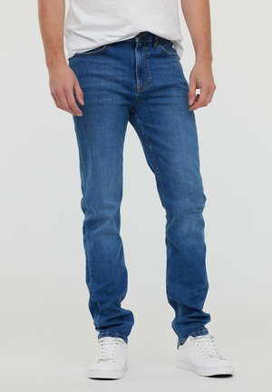 Blauwe denim jeans met een slim fit, typisch vijf-pocket ontwerp en contrasterende stiksels. Gecombineerd met witte sneakers.