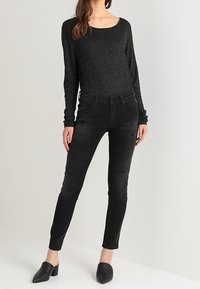 Top negro de manga larga con motas plateadas, combinado con jeans skinny negros con detalles de panel. Footwear son mule negros.