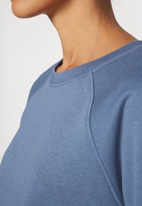 Sudadera de algodón azul con cuello redondo, que presenta una textura sutil y mangas raglán, destacando un diseño clásico y casual.