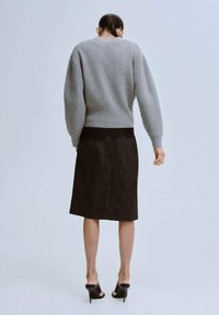 Šedý pletený svetr v kombinaci s tmavou džínovou sukní po kolena a černými sandály na podpatku, pohled zezadu na světlém pozadí.