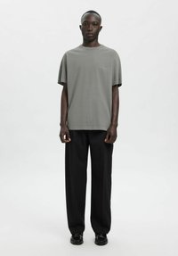 Hall hallist puuvillast lühikeste varrukatega T-särk, ümmarguse kaelusega ja diskreetse brändinguga; kantud koos lahtiste, mustade pükste ja mustade kingadega.