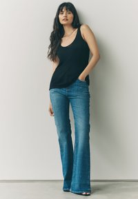 Sort ribbet tanktop kombineret med blå flare jeans. Glat stof øverst, struktureret denim med subtil tekstur, ankel-længde med flaret kant.