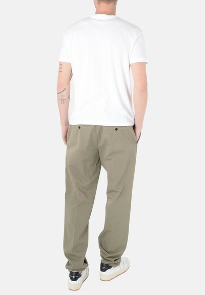 T-shirt bianco a maniche corte abbinato a pantaloni verde oliva chiaro. Le scarpe sono nere e bianche con una suola texturizzata. Le tasche sono visibili sui pantaloni.
