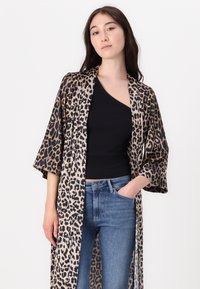 Kimono leopardato con apertura frontale, maniche corte e tessuto leggero. Indossato con un top nero e jeans in denim blu.