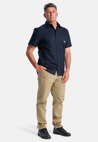 Donkerblauw overhemd met korte mouwen en een borstzak, gecombineerd met beige broek en zwarte sneakers, met een gladde stoftextuur.