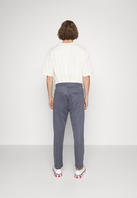 Gray sweatpants with a relaxed fit, elastic waistband, and two back pockets, paired with a white short-sleeve t-shirt and white shoes.