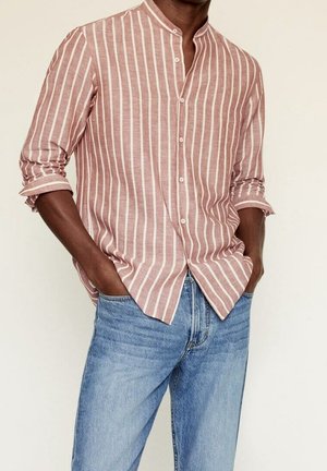 Camicia a maniche lunghe a righe rosa e bianca, con colletto alla mandarino e chiusura con bottoni. Abbinata a jeans di jeans blu chiaro.