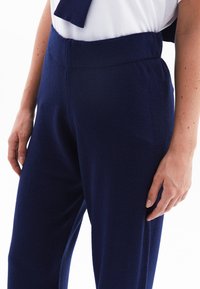 Marineblauwe, zachte stofbroeken met een brede tailleband en een relaxte pasvorm, met een gladde textuur en minimale stikseldetails.