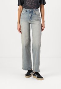 Hemelsblauwe denim wijde jeans met een hoge taille, duidelijke vervaging en subtiele slijtage. Gecombineerd met een zwart graphic t-shirt en sneakers.